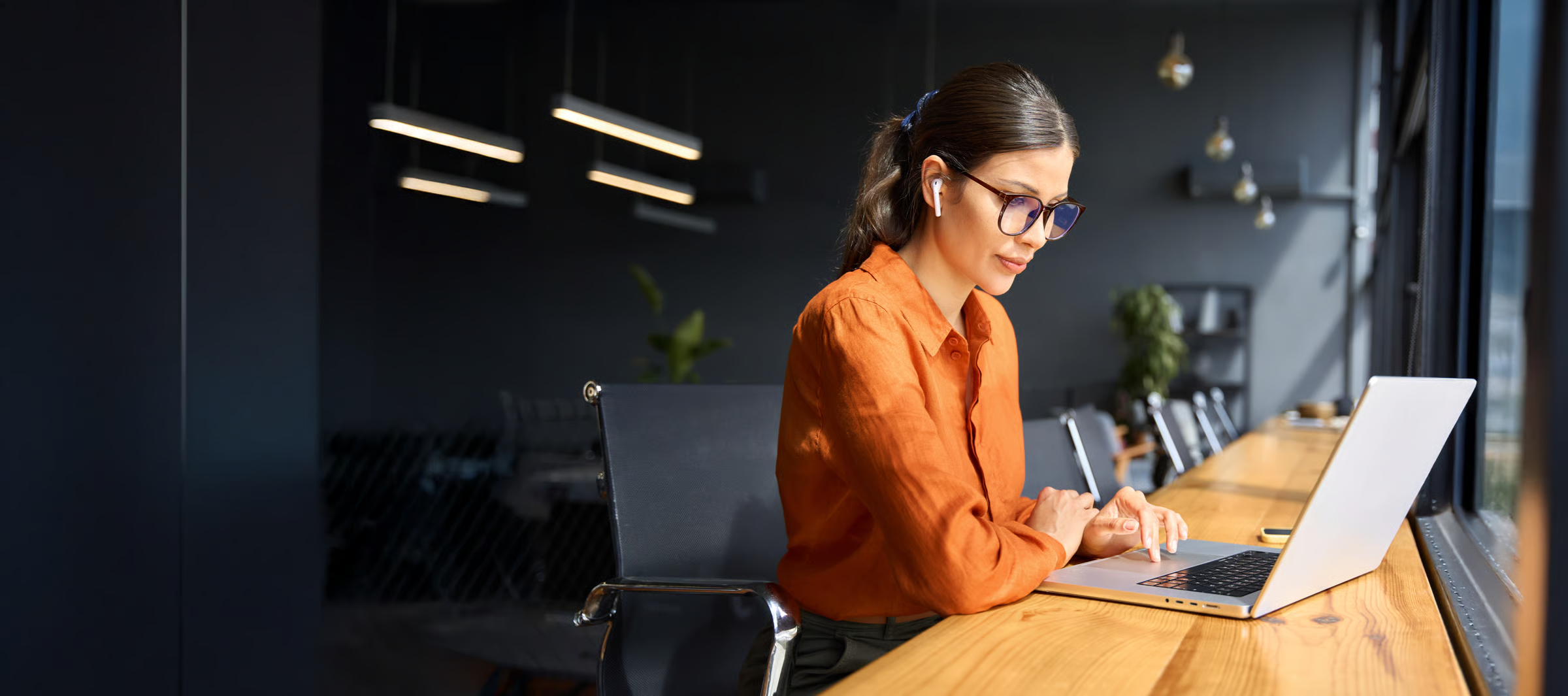Latin hispanic young business woman working on laptop computer at office desk with city view. Indian entrepreneur manager businesswoman using pc for work, learning at workplace. Banner, copy space